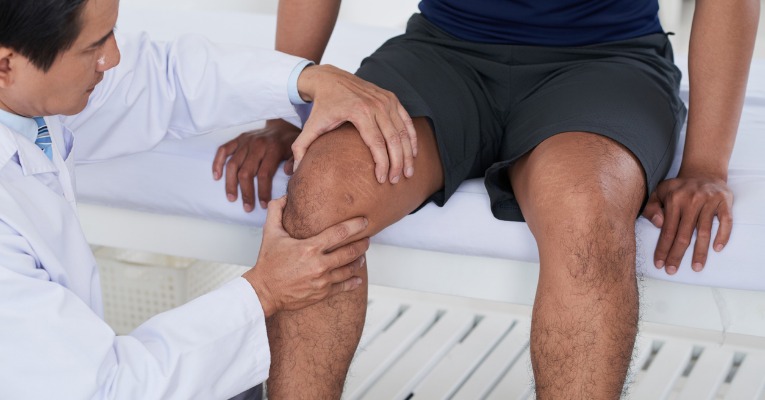 photo d'un médecin ou kinésithérapeute qui réalise un examen médicale clinique du genou d'un patient basketteur pour diagnostiquer une rupture des ligaments croisés