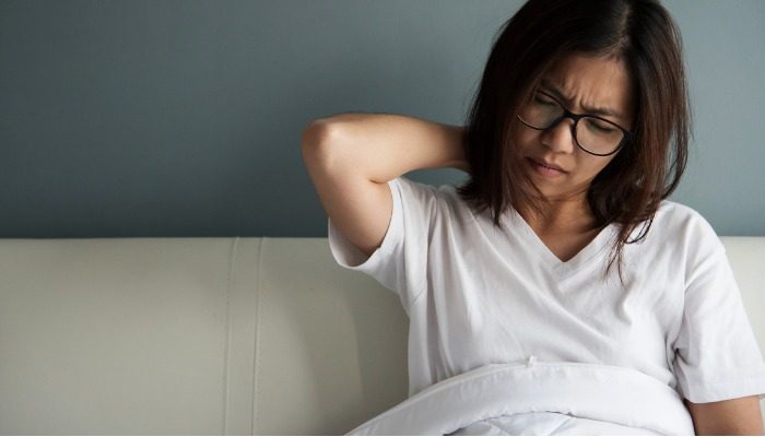 femme dans son lit qui se tient la nuque car le torticolis lui donne des douleurs cervicales la nuit