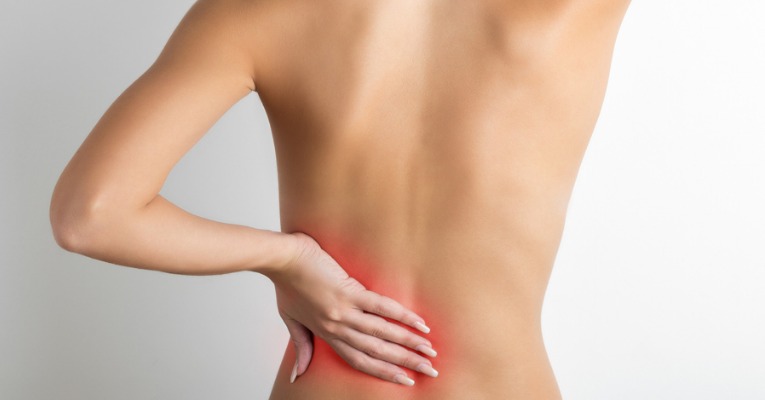 femme de dos se tenant le bas du dos pour cause de douleur lombaire type lumbago, lombalgie, hernie discale, sciatique