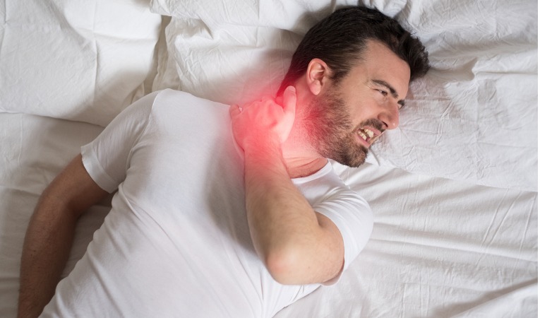 un homme allongé dans son lit qui souffre d'un torticolis au réveil après une mauvaise nuit