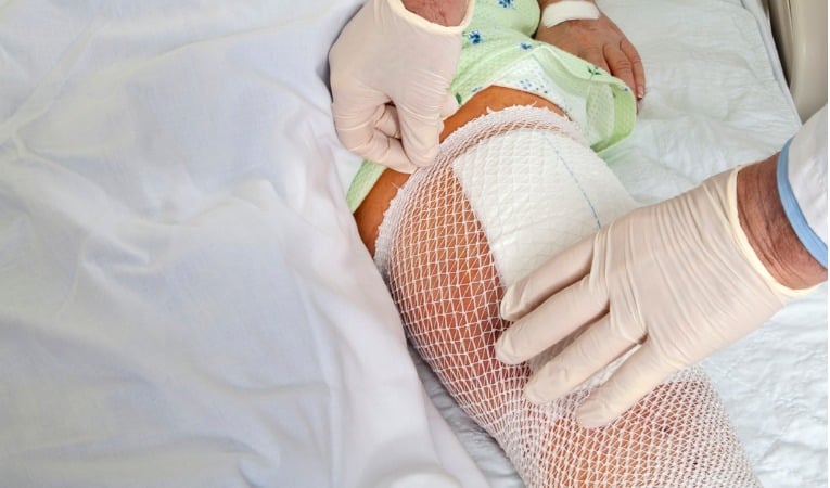 Un docteur retire le bandage post opératoire le lendemain après chirurgie de prothèse de genou