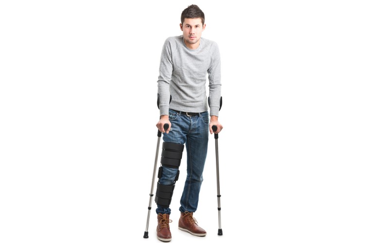 photo d'un jeune homme qui marche avec des béquilles et une attelle de zimmer d'immobilisation pour se soigner de sa rupture de ligament croisé antérieur du genou droit