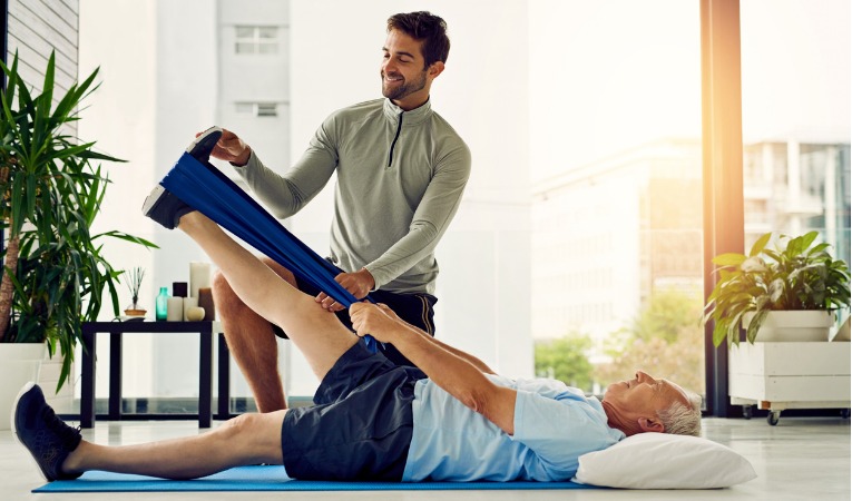 un kinésithérapeute explique un exercice de renforcement de la jambe durant une séance de rééducation avec un homme opéré d'une prothèse de hanche