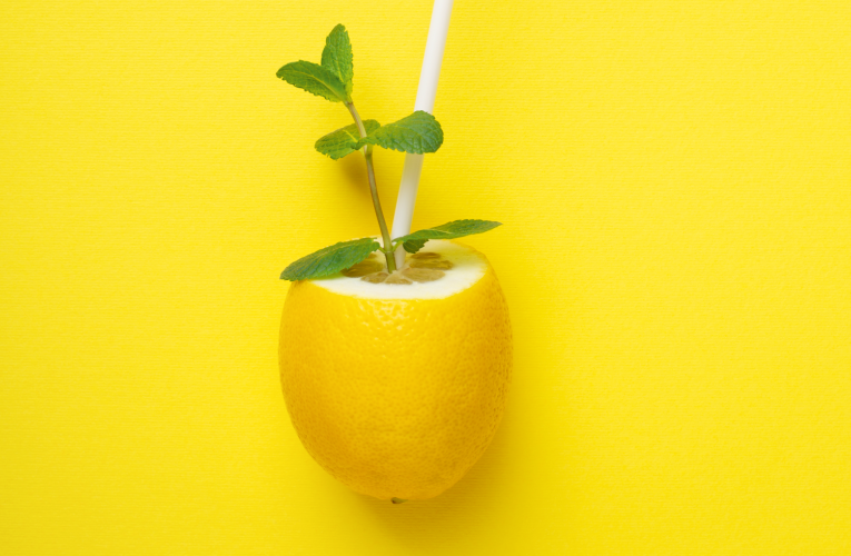 citron sur fond jaune avec une paille et une feuille de menthe dedans qui exprime le fait que boire du citron est bon pour la santé et healthy